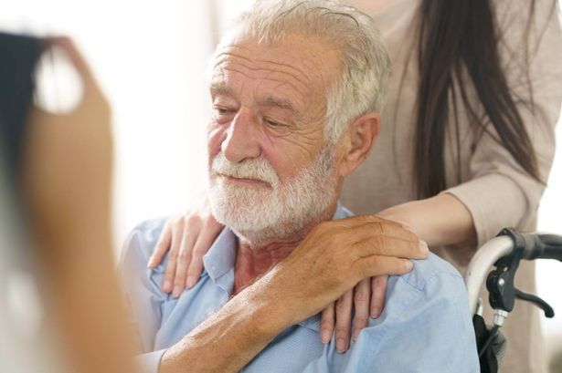 imported-0_An-elderly-man-in-a-wheelchair-smiles-slightly-as-he-holds-a-womans-hand.jpg
