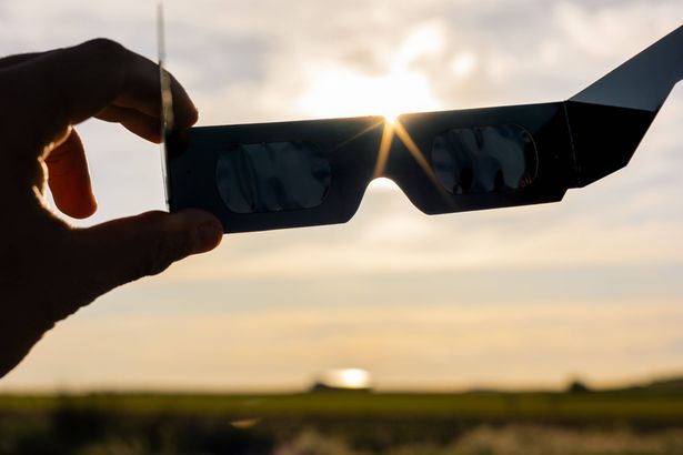 imported-1_Hand-holding-protective-solar-eclipse-glasses-looking-up-at-the-bright-sun-during-a-celestial-event-for-eye-protection.jpg