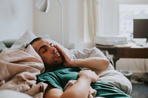 imported-0_A-man-wakes-up-on-a-sofa-surrounded-by-sheets-and-duvets-and-pillows-He-rubs-his-eyes-and-face-as-he-tries-to-rouse.jpg